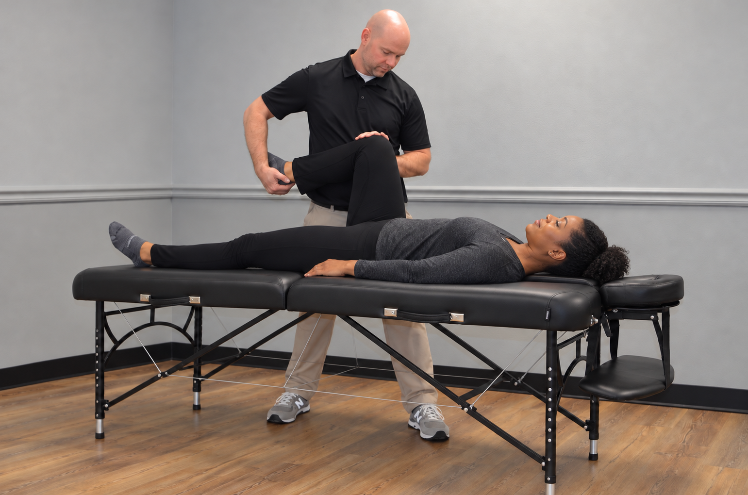 An assisted stretch session: a client lies on a treatment table while Jonathan guides her leg through a gentle stretch.